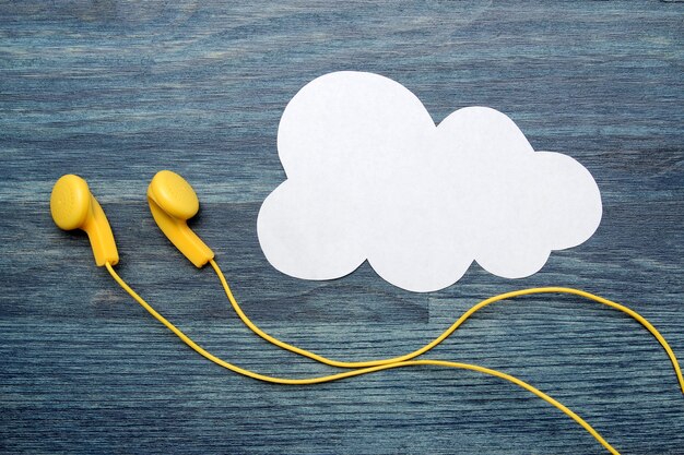 Small yellow headphones and a white cloud of paper on a blue wooden background. top view