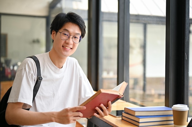 Smart Asian male college student wearing eyeglasses sits in a coffee shop with schoolbooks