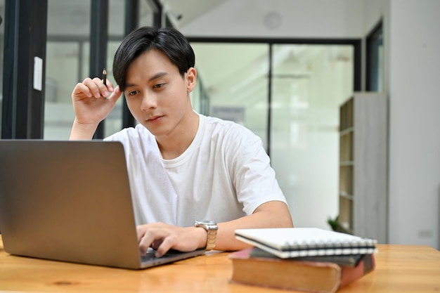 Smart Asian male concentrating doing his work project homework in campus library