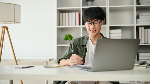 A smart Asian male office worker is taking notes on a notepad and focusing on his work