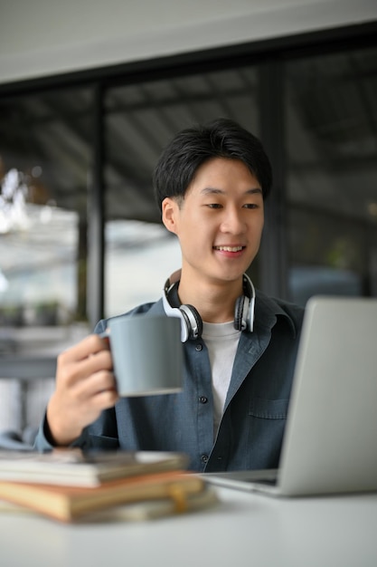 Smart Asian man remote working at the cafe sipping coffee and working on his project on laptop