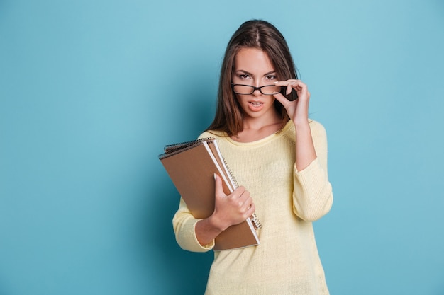 Smart beautiful woman looking at camera and touching glasses isolated on the blue background