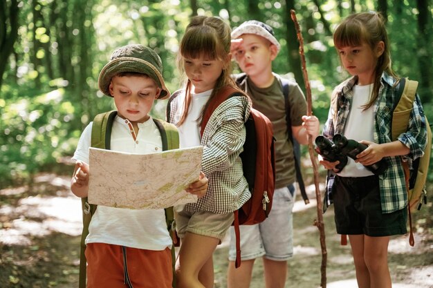 Photo smart boy is reading the map kids in forest at summer daytime together