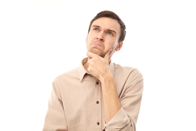 Smart brunette man in casual touches chin thinks doubts makes decision isolated on blue studio background