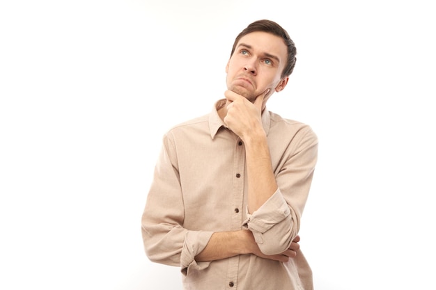 Smart brunette man in casual touches chin thinks doubts makes decision isolated on blue studio background