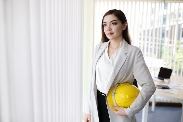 Smart business woman with suit hand hold engineer helmet standing in business office