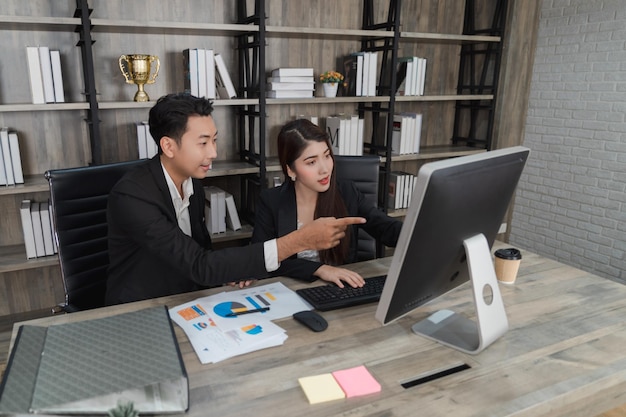 Smart businesswoman present data analysis on computer monitor to businessman collage in modern wooden office happy Asian business people working together looking at laptop success concept