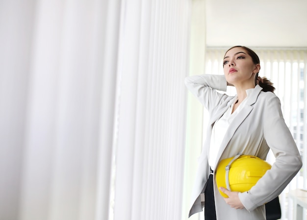 Smart businesswoman with suit hand hold engineer helmet standing in business office