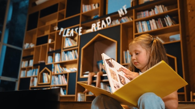 Photo smart caucasian girl picking reading a book while sitting at library erudition