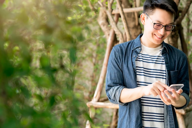 Smart cheerful asian glasses male hand use clear glass smartphone futuristic technology connectivity with background of beautiful green tree garden home concept