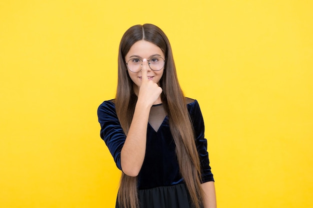 Smart girl child with long hair and eyeglasses on yellow background nerd