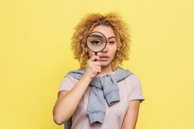 Smart girl is looking through a loupe. She is investigating something. Young woman is serious and calm.