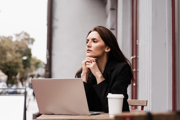 Smart girl student with laptop and cup of coffee study english online at linguistic school outdoor of cafe Attractive young woman have video communication lesson with teacher