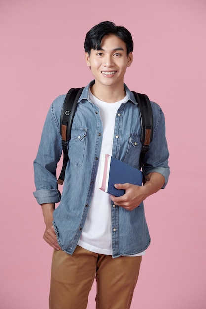 Smart guy student with backpack and bunch of books smiling at camera copy space for advertisement over pink background