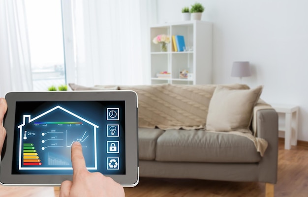 smart home and technology concept close up of male hands pointing finger to tablet pc computer with house settings on screen over living room background