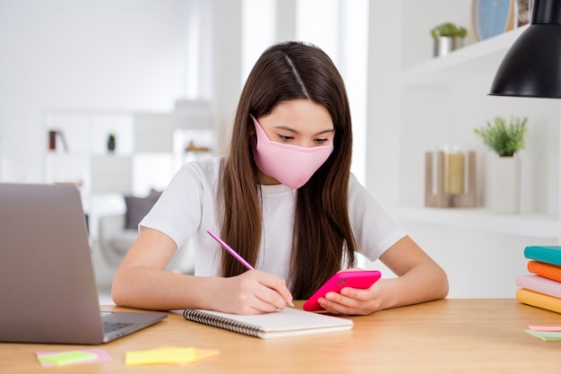 smart little lady in medical mask hold phone write homework