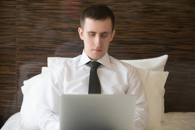 Smart man lying in bed typing on a laptop