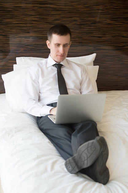 Smart man lying in bed typing on a laptop