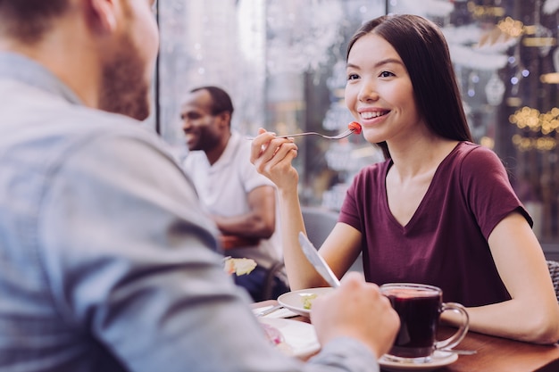 Smart pensive cheerful woman holding fork while looking at man and smiling