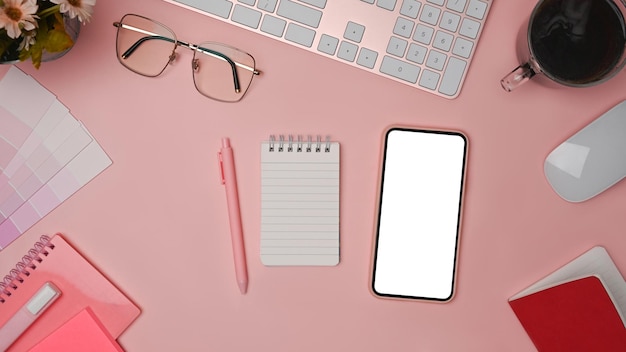 Smart phone coffee cup glasses and notebook on pink background Female workspace