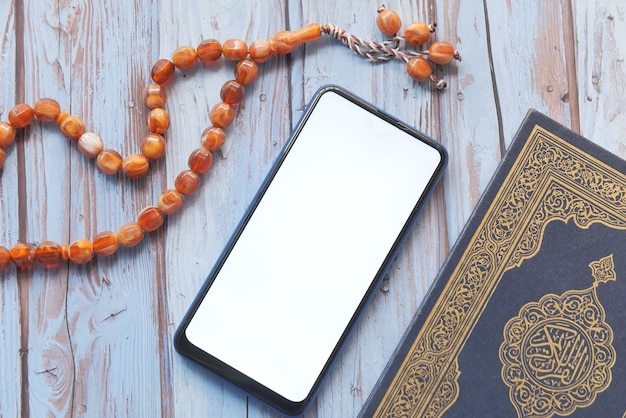 Smart phone, Holy book Quran and rosary on table,