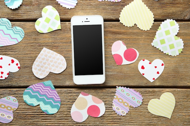 Smart phone with blank screen and hearts on old wooden table