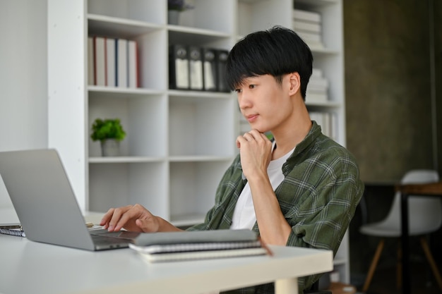 A smart and professional Asian male office worker focuses on his work on his laptop