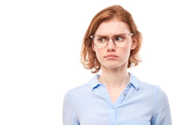 Smart redhead girl in business shirt and glasses grimacing and biting lips thinks doubts makes decision isolated on white studio background