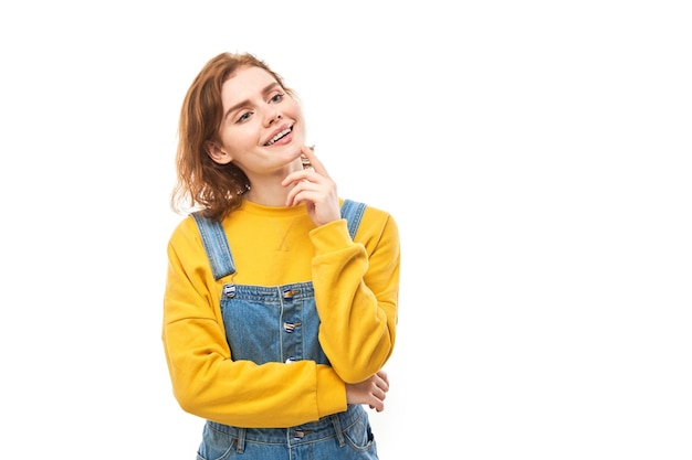 Smart redhead girl in casual holding chin thinks doubts makes decision isolated on white studio background