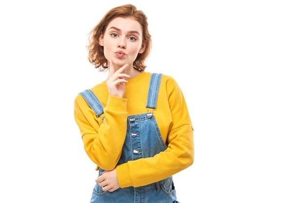 Smart redhead girl in casual holding chin thinks doubts makes decision isolated on white studio background