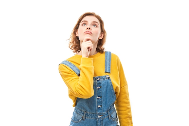 Smart redhead girl in casual holding chin thinks doubts makes decision isolated on white studio background