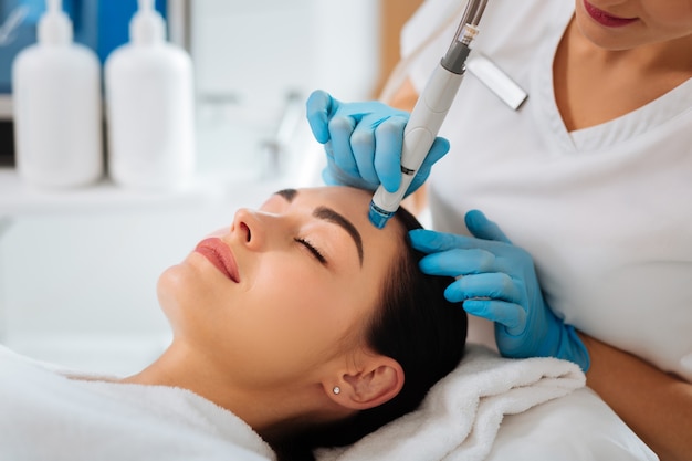 Smart skilled cosmetologist using a modern device while doing hydrafacial procedure