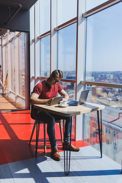 Smart software developer sitting at desktop in coworking space with laptop and creating publishing idea using netbook for messaging and networking during freelance work