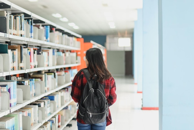 Smart student in casual style wearing backpack walking around the library while looking for a book