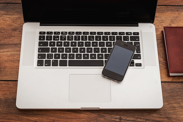 Smart technologies - smart solutions. Top view of laptop with mobile phone laying on the wooden desk