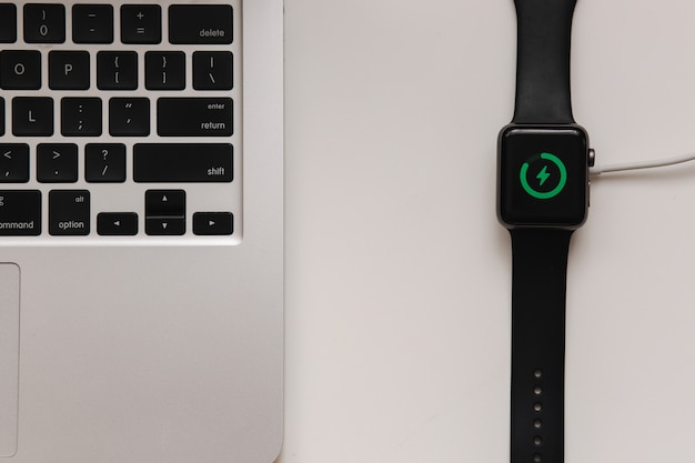 Smart watch on wireless charging with on-screen charging indicator. Work place near at the laptop. Top view. Place for text.