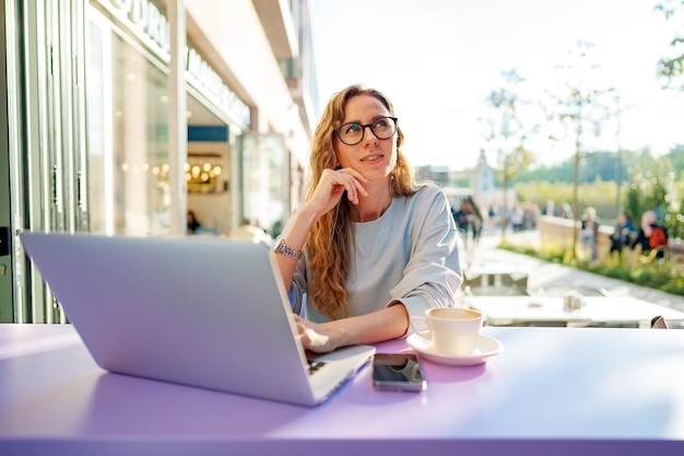 Smart woman in glasses sitting in cafe using laptop