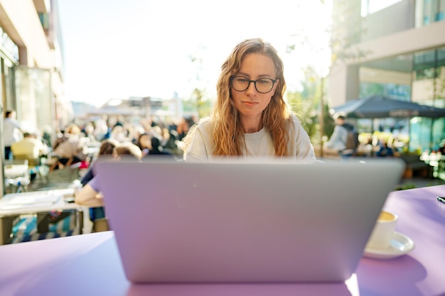 Smart woman in glasses sitting in cafe using laptop