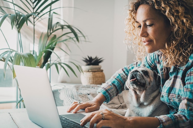 Smart working at home with female and her puppy working on computer together in friendship and love Cheerful happy woman write on laptop with a dog on her legs Concept of domestic animals lifestyle