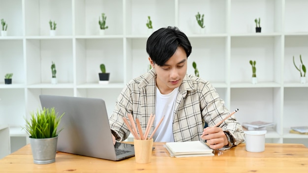 Smart young Asian male college student writing something on notebook