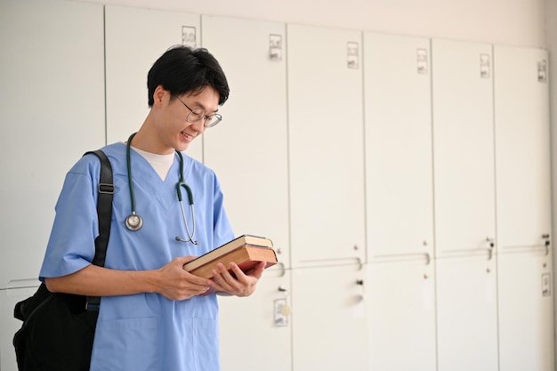 Smart young Asian male medical student in a uniform with medical books and backpack