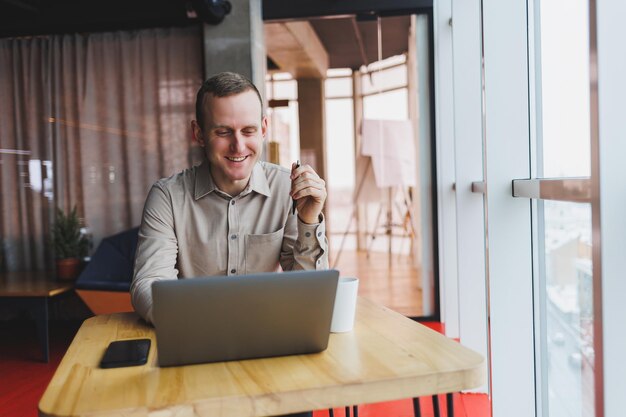 Smart young man looking for information on a website and working as a freelancer on developing a graphic project on a modern laptop using a wireless internet connection in a cafe interior