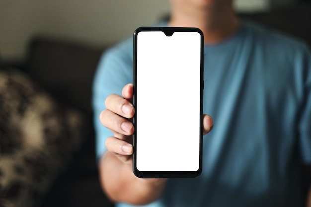 Smartphone blank screen presentation A young man is holding a phone with a white empty screen mockup a man is wear blue tshirt in living room at home