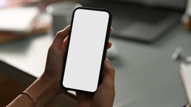 Smartphone empty white screen mockup for montage graphic image is in a womens hands over office desk