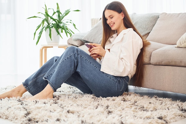 Smartphone in hands Young woman in white shirt and jeans is at home