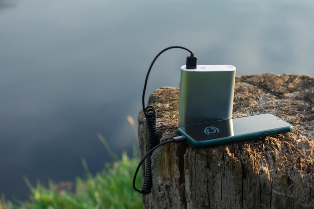 Smartphone is charged using a portable charger. Power Bank charges the phone outdoors with a backpack for tourism in the background of nature and the river.