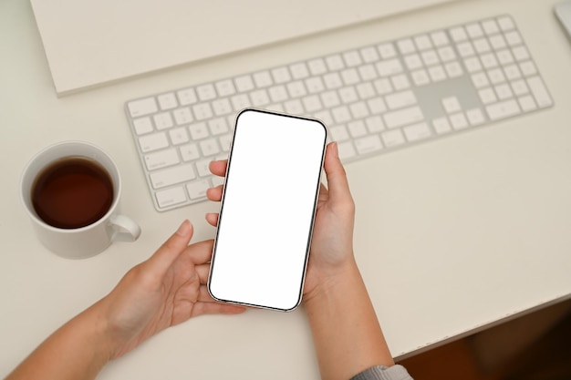 Smartphone mockup is in a woman's hands over modern minimal white office desk top view