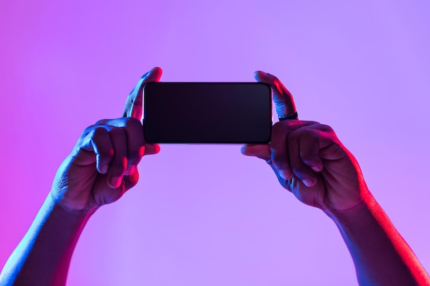 Smartphone screen mockup Closeup of young black man holding blank mobile device recommending new app in neon light