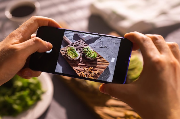 Smartphone taking picture from organic healthy sandwiches with avocado Man hand