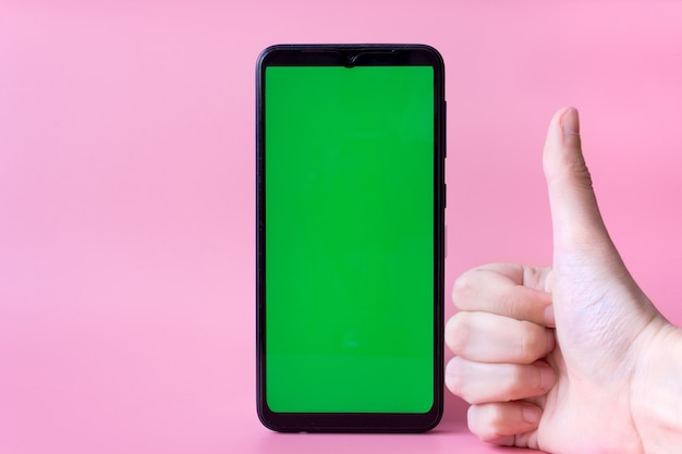 A smartphone in a vertical position with a green screen on a pink background and a hand with a thumb up. Chroma key. Mock up.